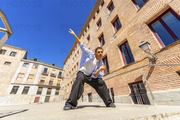 Young man actively posing or dancing in a dynamic stance on a sunny urban street, expressing