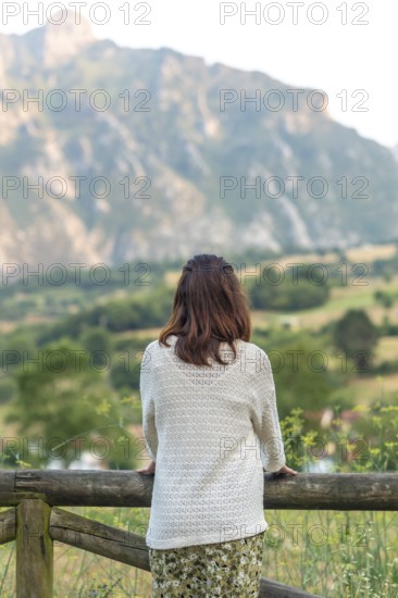 Woman leaning on a wooden fence, admiring the breathtaking view of picu urriellu, a stunning peak