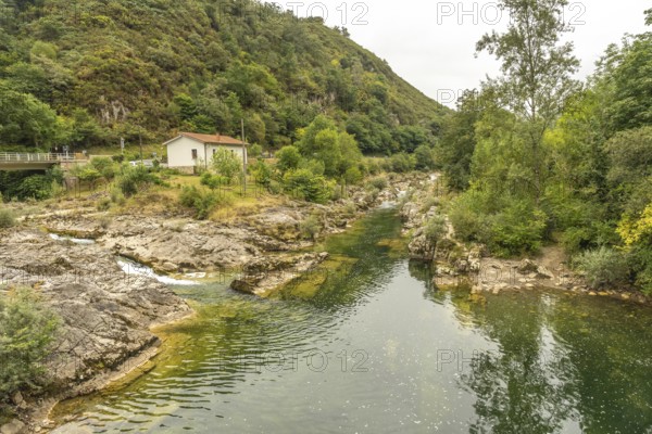 Sella river meandering through a rocky riverbed, surrounded by lush vegetation, trees, and a small