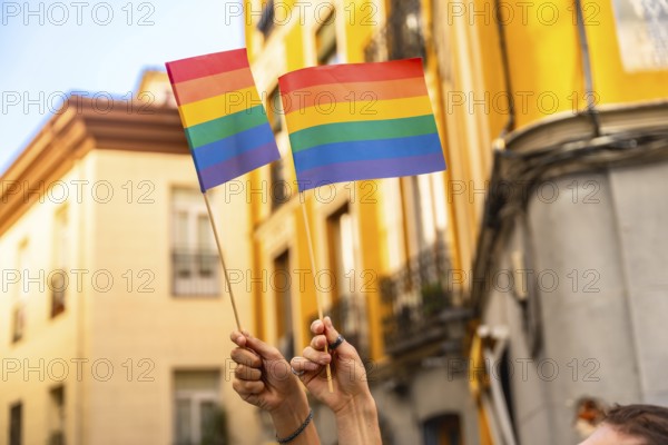 Hands are raising two small rainbow flags, symbolizing lgbtq plus pride, diversity, and equality,