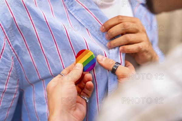 Young couples hands pinning a rainbow pride flag button to a striped shirt, close up symbolizing