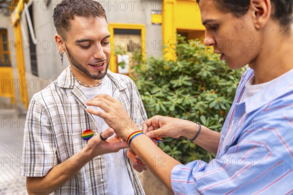 Two men clasp hands and put on rainbow flag bracelets outdoors, celebrating love, pride and