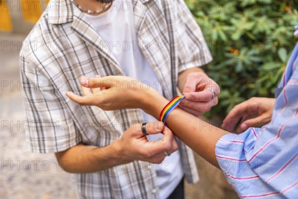 Two hands fastening a colorful rainbow bracelet on a wrist outdoors, symbolizing pride, love and