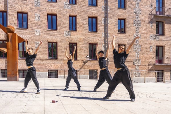Four young male and female dancers performing a synchronized urban choreography with arms raised,