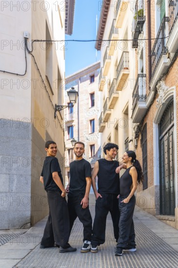 Group of diverse dancers wearing black casual clothing are posing and smiling while looking at the