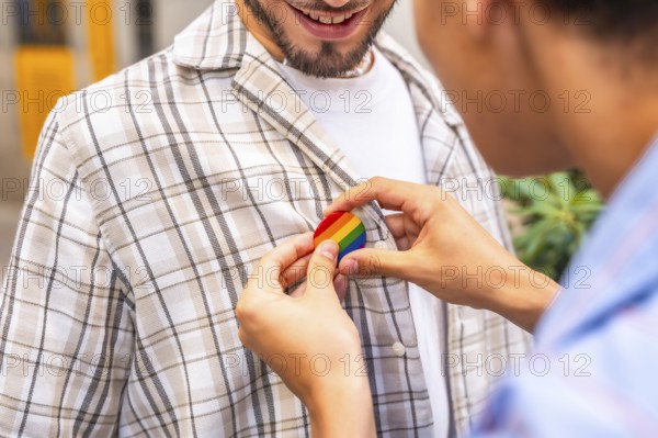Gay partner pinning a rainbow pride badge to their partner's plaid shirt, close up of hands showing