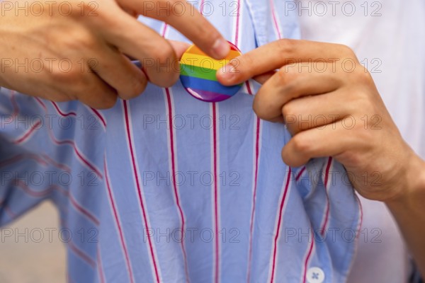 Person's hands carefully pinning a rainbow pride flag button onto a blue and white striped shirt,