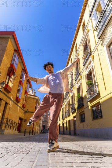 Young man actively posing and dancing on a cobblestone city street in historic european