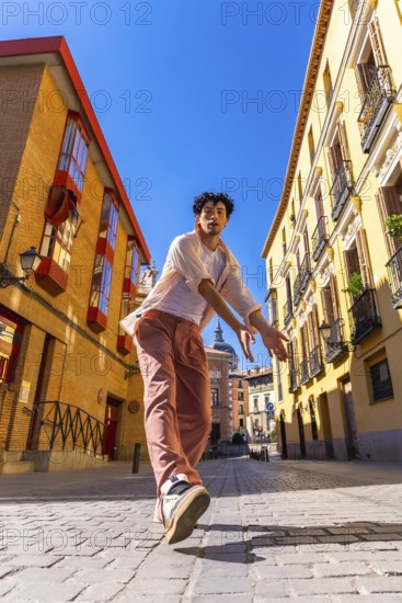 Young man striking a dynamic urban dance pose on sunlit cobblestones in madrid, radiating energy,