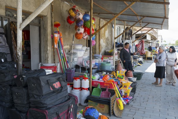A shopping street with toys and household goods, meat hanging in front of the door, customers