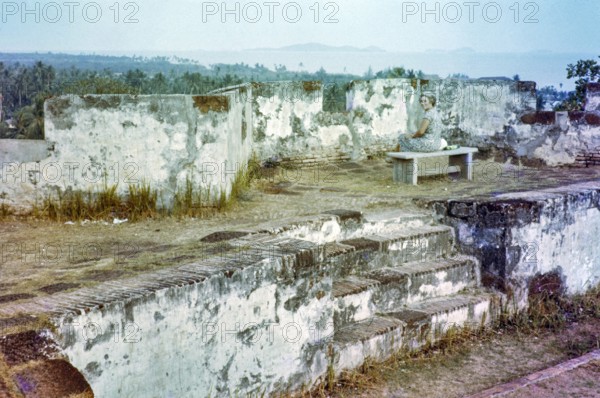 British expatriate tourist woman sitting on bench by walls ruin thought to be Malacca or Melaka,