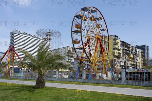 A colourful amusement park with a Ferris wheel against an urban backdrop under a clear sky,