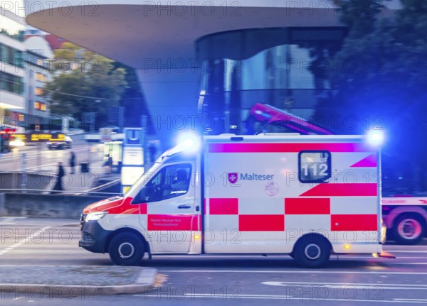 Ambulance of the BOS organisation Malteser with blue lights in an urban environment. Pulling along.
