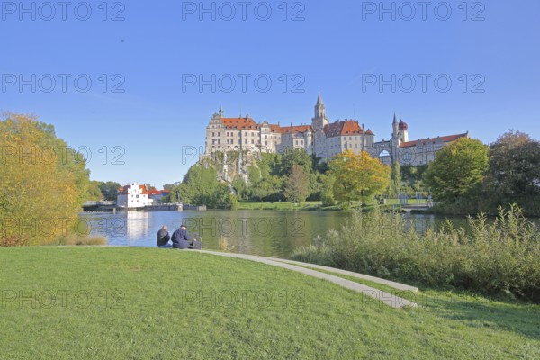Hohenzollern Castle and Danube, river bank with autumn colours and two seated people, landmark,