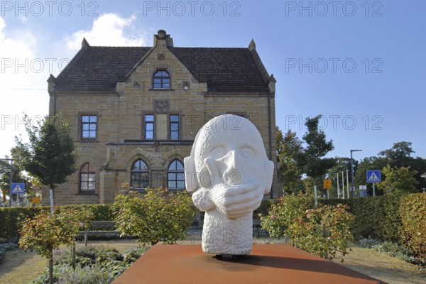 Sculpture head with headphones and hand for in front of the mouth, ambivalent symbolism for peace,