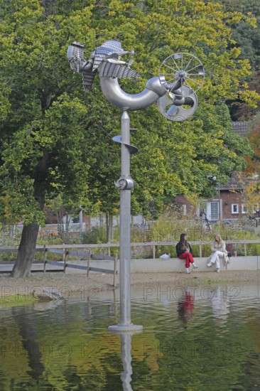 Sculpture Birdman by Albert Sous and two seated woman in conversation, people, pond, modern art,