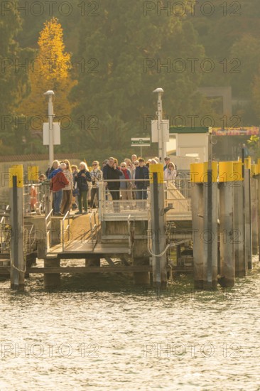 People waiting at a jetty surrounded by trees with autumn colours, Mainau Island, Lake Constance,