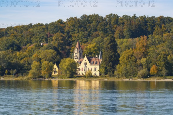 A picturesque castle on the shore of a lake surrounded by autumnal trees with a clear sky,
