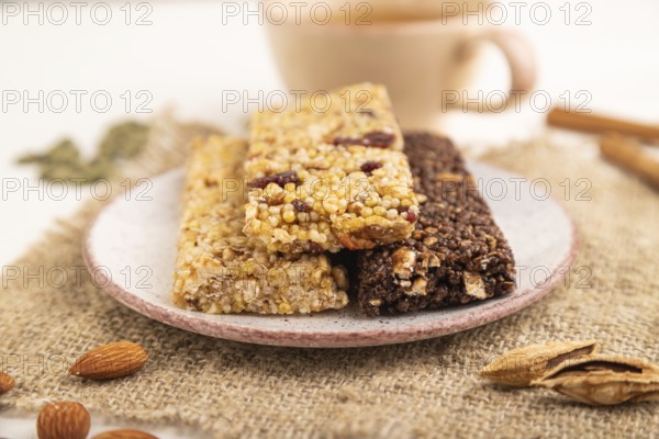 Granola bars with caramel, nuts, flakes in ceramic plate on white wooden background, beige linen