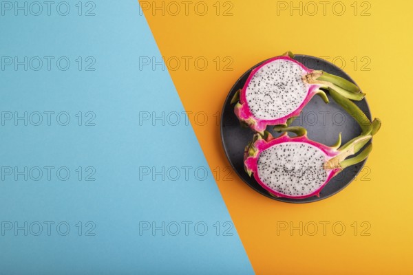 Ripe Pitaya on blue plate on blue and orange pastel paper background, top view, flat lay, copy