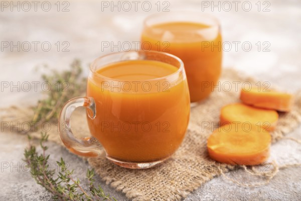Two glasses with carrot juice, on brown concrete background and linen textile. Diet, healthy eating