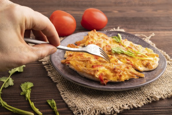 Baked chicken meat with cheese and tomatoes with hand on brown wooden background and linen textile.