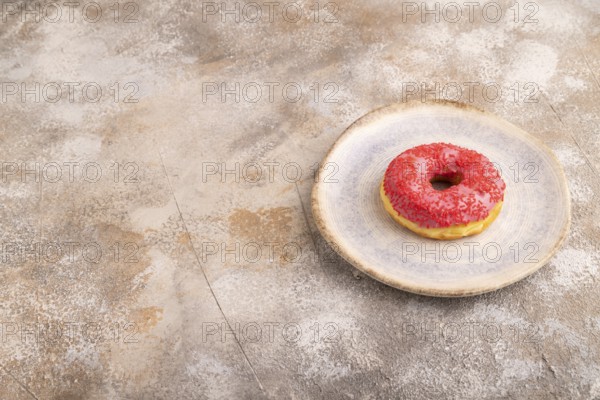 Pink Donut with sprinkles on blue ceramic plate on brown concrete background, side view, copy