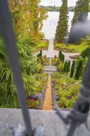 View through a gate onto a well-kept garden path leading to the lake, surrounded by autumn trees,