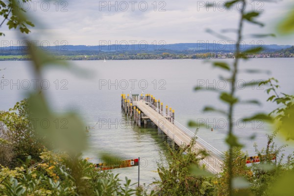 View of a long jetty leading into a calm lake with a cloudy sky in the background, Mainau Island,