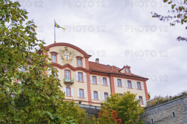 A magnificent building with a flag in the foreground, surrounded by autumnal greenery, Mainau
