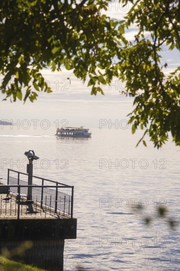 A boat passes by on a calm lake, visible from a binocular viewpoint next to a jetty, Überlingen,