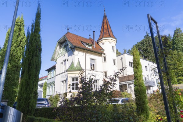 Historic building with tower and pointed roofs, surrounded by trees under a clear sky, Überlingen,