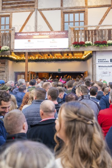 Crowds of people standing in front of the entrance to a wooden building, expectant atmosphere,
