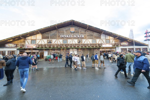 Visitors move in front of a large wooden building, lively atmosphere, Cannstatter Wasen folk