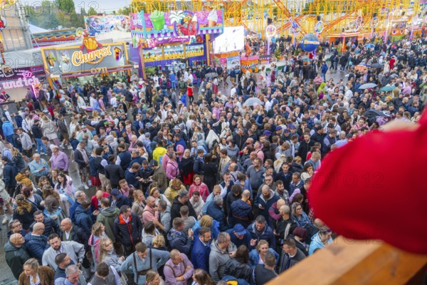 Dense crowd on a busy fairground with colourful attractions all around, Cannstatter Wasen funfair,