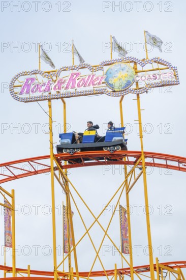 Roller coaster car on rails with rock and roller lettering and colourful flags, Cannstatter Wasen