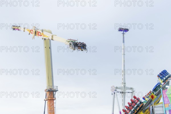 View of thrill rides with people high above and other attractions in the background, Cannstatter
