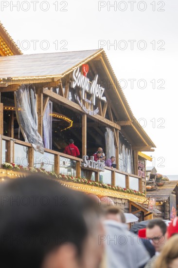 People standing on a balcony of a Bavarian wooden building with a glass front, Cannstatter Wasen