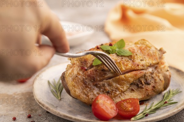Fried Turkey Thigh with spices and rosemary on plate with hand on brown concrete background and