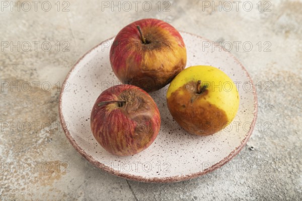 Decaying, Rotting apples on ceramic plate on brown concrete background. Side view, close up,
