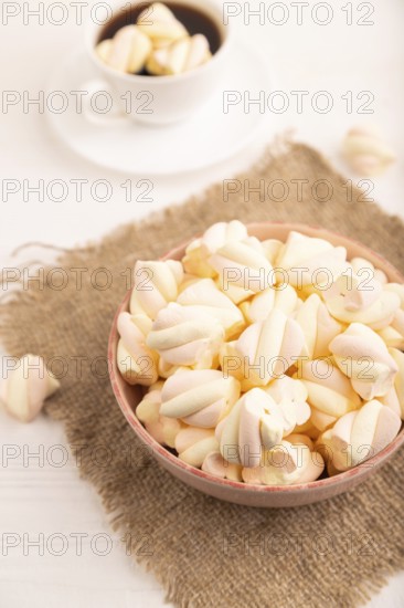 Orange and pink marshmallow in ceramic bowl on white wooden background, side view, close up,
