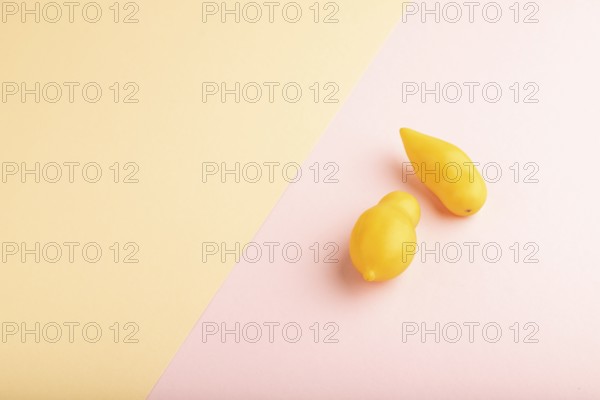 Yellow tomatoes on pink and orange pastel paper background. Side view, copy space, flat lay.