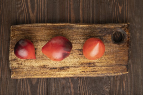 Red Heart shape tomatoes on cutting board on brown wooden background. Top view, copy space, flat