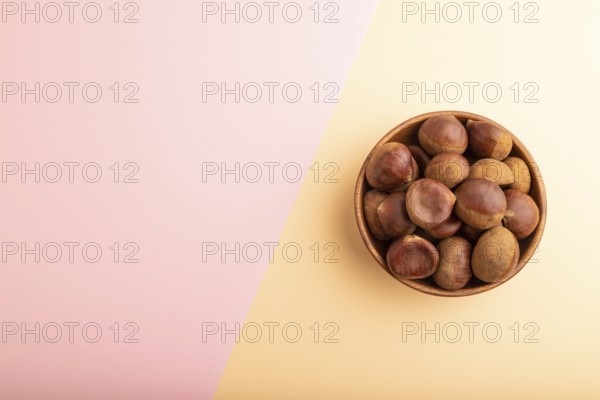 Wooden bowl with raw edible ?hestnuts on pink and orange paper pastel background, top view, flat