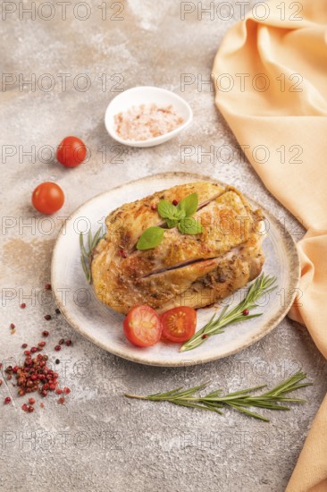 Fried Turkey Thigh with spices and rosemary on plate on brown concrete background and orange linen
