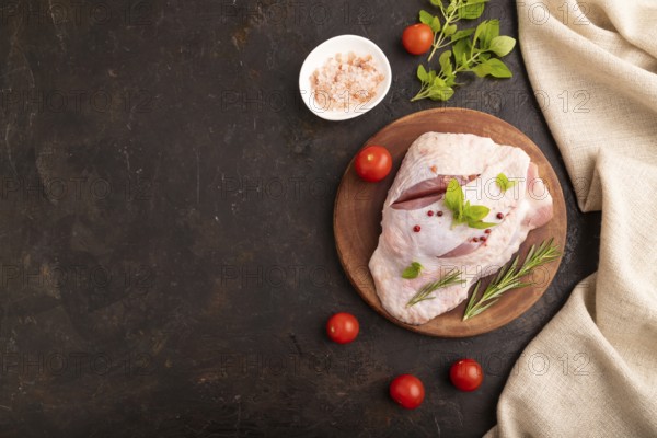 Raw Turkey Thigh with spices and rosemary on cutting board on black concrete background and linen