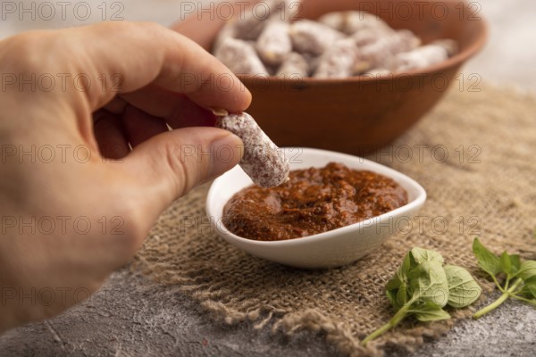 Small smoked Chicken sausages in clay bowl with hand on brown concrete background and linen textile
