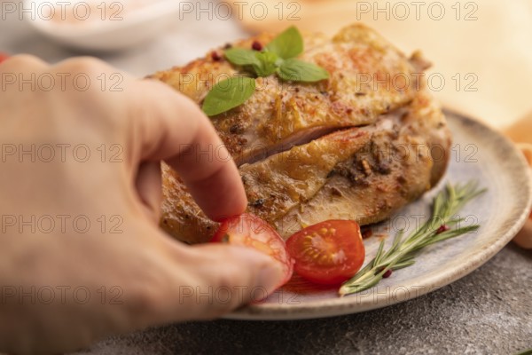 Fried Turkey Thigh with spices and rosemary on plate with hand on brown concrete background and