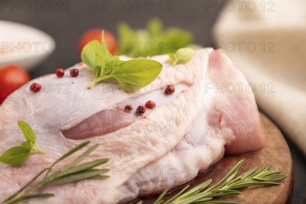 Raw Turkey Thigh with spices and rosemary on cutting board on black concrete background and linen