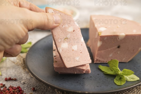 Mortadella sausage with hand on plate with pepper and herbs on brown concrete background and linen